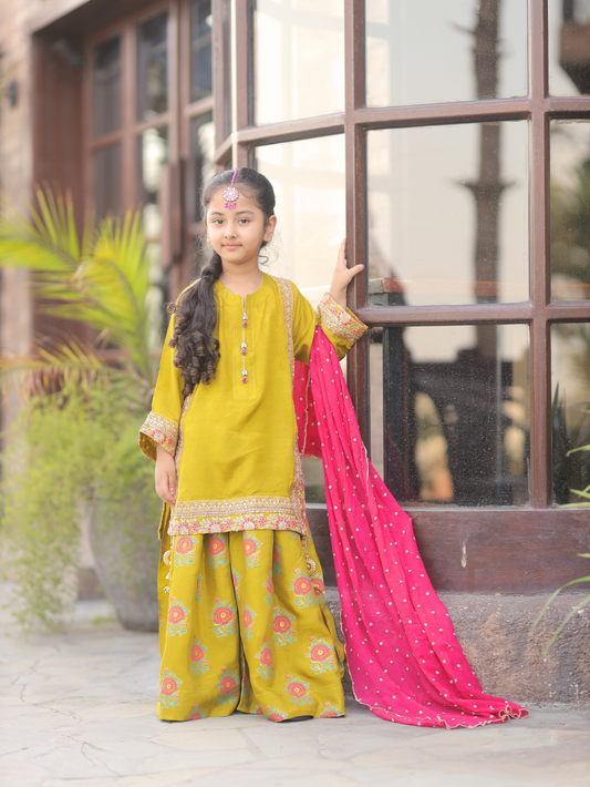 A young girl wearing a green and pink traditional outfit with floral patterns and a dupatta with gold detailing.
