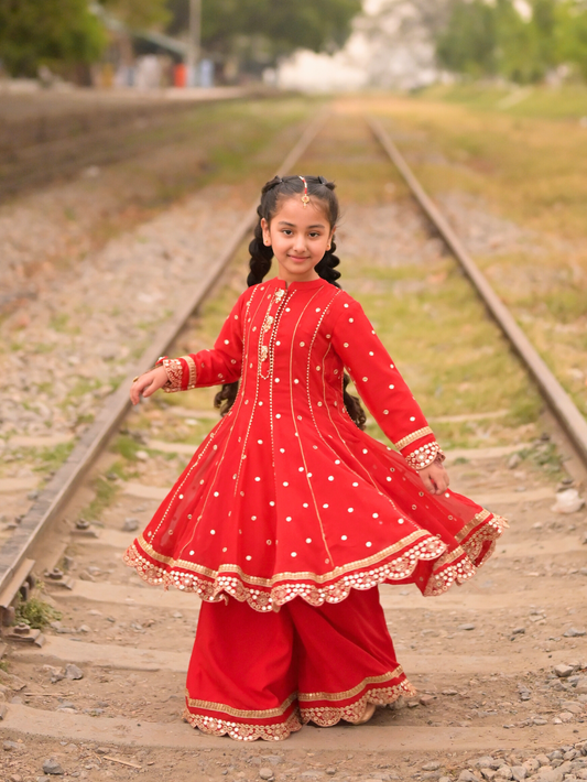 Young girl in a red traditional outfit standing on railway tracks with a blurred background